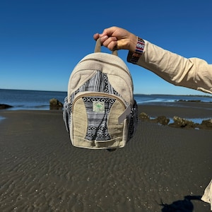 May include: A beige hemp backpack with black and white patterned fabric. The backpack has a small green leaf logo with the text "WELLNESS" on it.