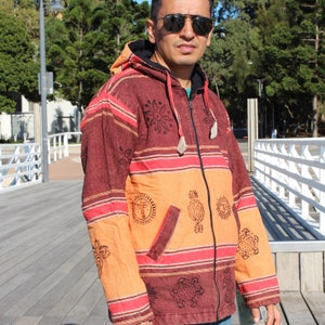 May include: A hooded jacket with a zipper closure and a striped pattern in shades of orange, red, and brown. The jacket features various printed designs, including suns, flowers, and other geometric shapes.