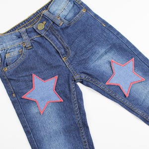 May include: Blue denim jeans with two red star-shaped patches. The stars are made of a blue denim fabric.