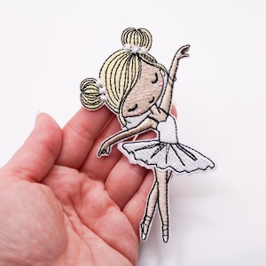 May include: Embroidered patch of a ballerina in a white tutu and pointe shoes. The ballerina has blonde hair in a bun and is in a graceful pose. The patch is designed in a cartoon style and is suitable for clothing or accessories.