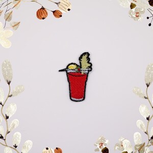 May include: Embroidered iron-on patch of a red cocktail with a lime wedge and a cherry on top.