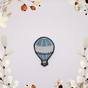 Op de afbeelding: Een geborduurde patch met een blauwe en witte luchtballon met een bruine mand.