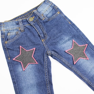 May include: Blue denim jeans with two black star-shaped patches outlined in pink.