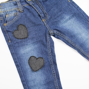 Pode incluir: Jeans azul denim com dois patches em forma de coração preto.