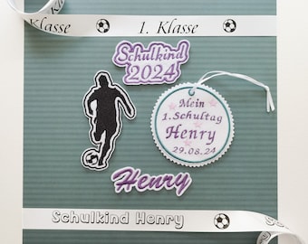 May include: A green card with a white ribbon that says "1. Klasse" and a soccer ball icon. There are several embroidered patches on the card, including a soccer player, a circle with the text "Mein 1. Schultag Henry 29.08.24", and the name "Henry" in purple lettering. The text "Schulkind Henry" is also printed on the card.