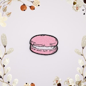 Può includere: Un macaron rosa ricamato con ripieno bianco. Il macaron è un dolce francese popolare.