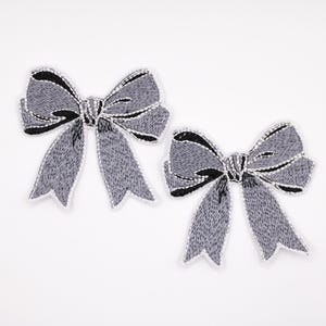 May include: Two gray embroidered bow appliques with black and silver accents. The bows have a textured appearance and are set against a white background. These decorative bows are suitable for crafts and embellishments.