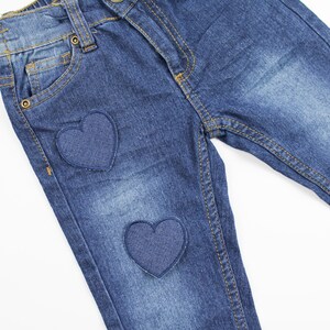 May include: A pair of blue denim jeans with two heart-shaped patches sewn on the front.