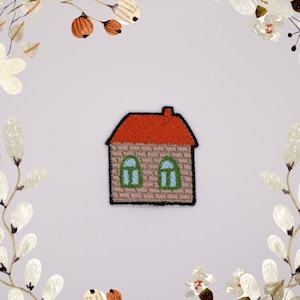 May include: Embroidered iron-on patch of a small house with a red roof, two windows, and a brown brick exterior.