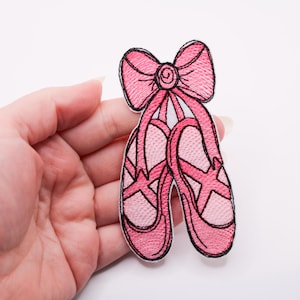 Può includere: Toppa ricamata raffigurante un paio di scarpette da ballo rosa con un fiocco abbinato. La toppa ha un contorno nero ed è posta su uno sfondo bianco. Le scarpette da ballo sono di colore rosa chiaro.