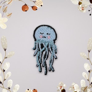 Puede incluir: Un parche de hierro azul bordado de una medusa de dibujos animados con una cara sonriente y los ojos cerrados. La medusa tiene un cuerpo azul claro y tentáculos azul oscuro.