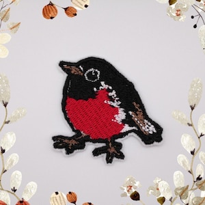 May include: Embroidered iron-on patch of a red-breasted robin with black wings and a white belly. The bird is perched on a branch with its wings slightly spread.