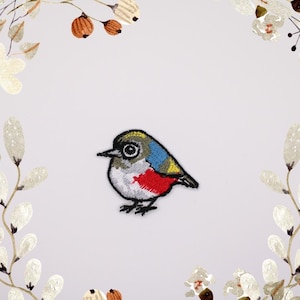 Pode incluir: Etiqueta bordada para passar a ferro com um pequeno pássaro colorido com um design cinza, branco, vermelho, azul e amarelo.