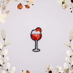 May include: Embroidered iron-on patch of a red cocktail drink in a glass with a cherry on top.