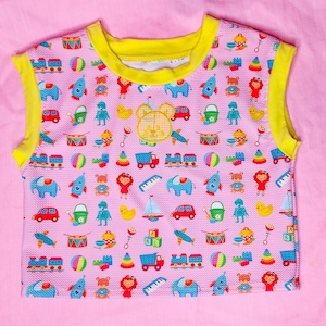 May include: Pink sleeveless top with a yellow trim, covered in a pattern of colorful toy illustrations. The design includes toy cars, trains, elephants, dolls, and more. A bear face is embroidered on the front.