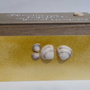 Pode incluir: Uma caixa de madeira com uma tampa dourada. A tampa tem o texto "Memories made together are special treasures" escrito nela. Há quatro conchas na tampa.
