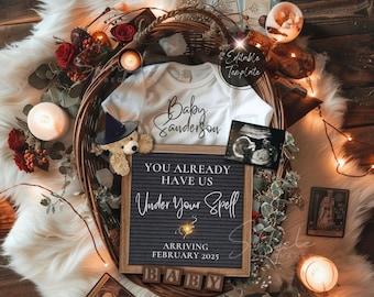 May include: A black letter board with the text "You already have us under your spell" and "Arriving February 2025". A white onesie with the text "Baby Sanderson" is in the background. The letter board is surrounded by candles, lights, and other decorations.