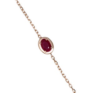 Pode incluir: Um delicado colar em ouro rosa com uma única gema de rubi oval. O rubi é fixado em uma moldura e suspenso por uma corrente fina. Uma joia simples, mas elegante.