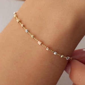 Könnte beinhalten: Ein zartes Goldarmband mit kleinen runden Perlen. Die Perlen sind eine Mischung aus Gelb-, Weiß- und Roségold.