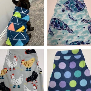 May include: A dog wearing a navy blue fleece dog coat with a geometric pattern of triangles in shades of blue, yellow, orange, and green. Also shown are fleece dog pants with turtle, chicken, and polka dot patterns.