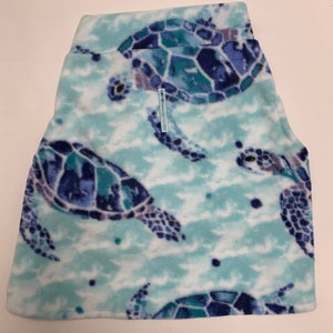 May include: A pair of fleece shorts featuring a sea turtle pattern. The shorts have a light blue background with a repeating pattern of blue and teal sea turtles. The shorts have a wide waistband and a small, light blue tag.