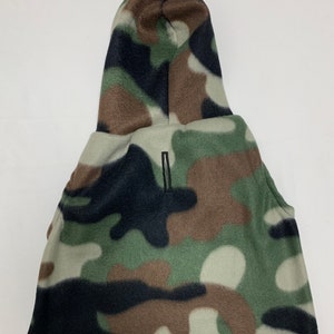 May include: A camouflage-patterned hood with a zipper closure. The hood features a mix of green, brown, black, and white shapes. The hood is made of a soft, fleece-like material.