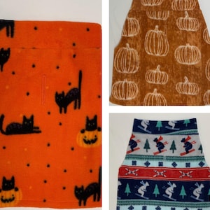 May include: Three fleece fabric pieces. One is orange with black cat and pumpkin graphics. Another is brown with white pumpkin graphics. The third is blue, red, and white with skiers and trees.