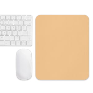 Puede incluir: Una configuración de computadora con un teclado blanco, un ratón blanco y una alfombrilla de ratón rectangular de color naranja claro. El teclado tiene una distribución estándar con teclas negras y letras blancas. El ratón es elegante y minimalista.