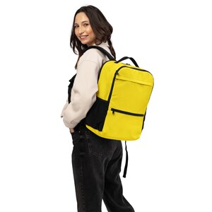 Peut inclure: Un sac à dos jaune vif avec des accents noirs, comprenant des poches latérales en filet, des bretelles réglables et deux compartiments avant zippés. Le sac présente une forme rectangulaire structurée avec une poignée supérieure.