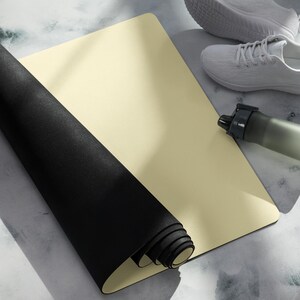 Peut inclure: Un tapis d'exercice rectangulaire présentant une surface supérieure lisse de couleur crème et un dessous noir texturé partiellement enroulé. Le tapis est placé à côté d'une paire de baskets blanches et d'une gourde gris foncé.