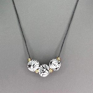May include: A black necklace with four white and black patterned beads. The beads have a gold accent.