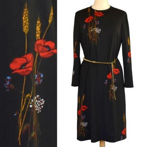 May include: Black long-sleeve dress with a floral design featuring red poppies, blue flowers, and wheat stalks. The dress has a gold-colored belt and is displayed on a mannequin.