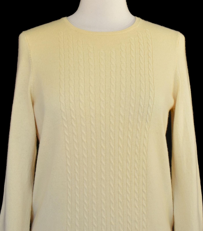 May include: A white ceramic mug with a black handle and the text "But First, Coffee" in a black, bold font. The mug is on a white surface.