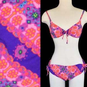 May include: A vintage bikini set with a vibrant floral pattern in pink, orange, and purple. The two-piece swimsuit features a triangle top with tie closures and matching bottoms with side ties. The fabric has a retro, psychedelic design.