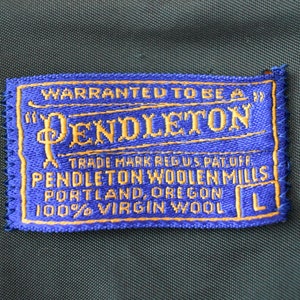 Puede incluir: Una etiqueta Pendleton azul y dorada con el texto "WARRANTED TO BE A" y "PENDLETON". La etiqueta tambi&eacute;n incluye "TRADE MARK REG US PAT OFF", "PENDLETON WOOLEN MILLS", "PORTLAND, OREGON" y "100% VIRGIN WOOL".