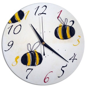 May include: White round clock with black hands and black Roman numerals. The clock face has three yellow and black bees with yellow wings.