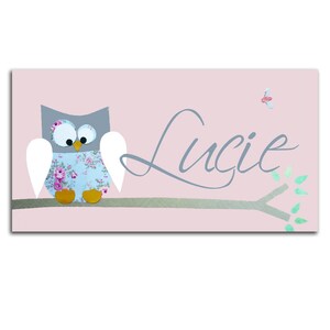 K&ouml;nnte beinhalten: Ein rosa Hintergrund mit einer grauen Eule mit wei&szlig;en Fl&uuml;geln, die auf einem Ast sitzt. Die Eule hat ein blaues und wei&szlig;es Blumenmuster auf ihrem K&ouml;rper. Der Name "Lucie" ist in grauer Kursivschrift auf dem Ast geschrieben.