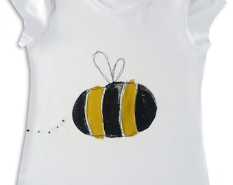 May include: White t-shirt with a black and yellow bee illustration. The bee has a simple, hand-drawn style and is centered on the shirt.