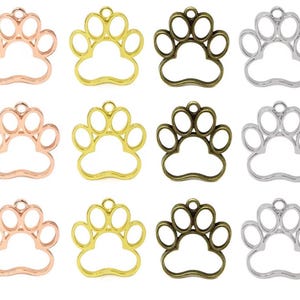 May include: A collection of twelve metal paw print charms arranged in a grid. The charms are available in four metallic finishes: rose gold, bright gold, antique bronze, and silver. Each charm features an open frame design with a small loop at the top.