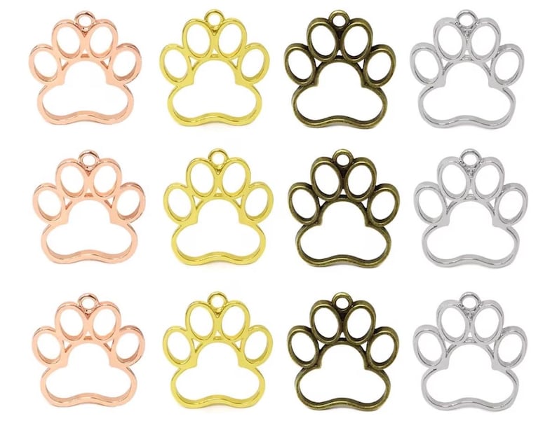 May include: A collection of twelve metal paw print charms arranged in a grid. The charms are available in four metallic finishes: rose gold, bright gold, antique bronze, and silver. Each charm features an open frame design with a small loop at the top.