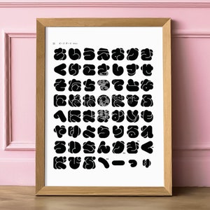 Op de afbeelding: Een ingelijste print met een raster van zwarte abstracte vormen op een witte achtergrond. De vormen doen denken aan gestileerde karakters of symbolen. De lijst is gemaakt van lichtbruin hout. De print wordt gepresenteerd tegen een roze muur.