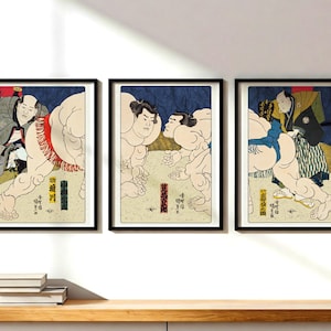 May include: Three framed prints of Japanese woodblock prints depicting sumo wrestlers in action. The prints are in black and white with red and blue accents. The prints are framed in black.