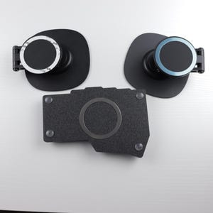 May include: Three black magnetic phone mounts. Two have a circular design with a black base and a rotating dial. The third is a dark gray, textured rectangular piece with a circular magnetic area.
