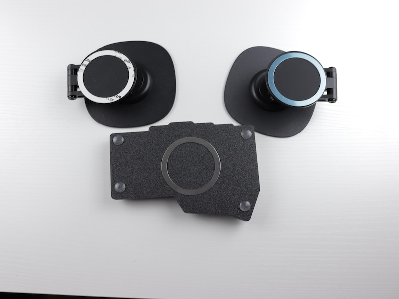 May include: Three black magnetic phone mounts. Two have a circular design with a black base and a rotating dial. The third is a dark gray, textured rectangular piece with a circular magnetic area.