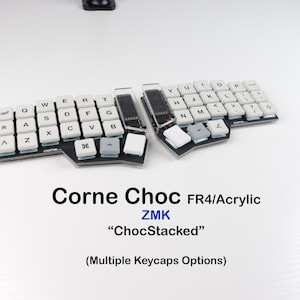 Könnte beinhalten: Eine geteilte ergonomische mechanische Tastatur mit weißen Tastenkappen auf einer schwarzen Basis. Der Text lautet: Corne Choc FR4/Acrylic, ZMK, ChocStacked, (Multiple Keycaps Options). Die Tastatur hat ein versetztes Layout mit sichtbaren Bauteilen.