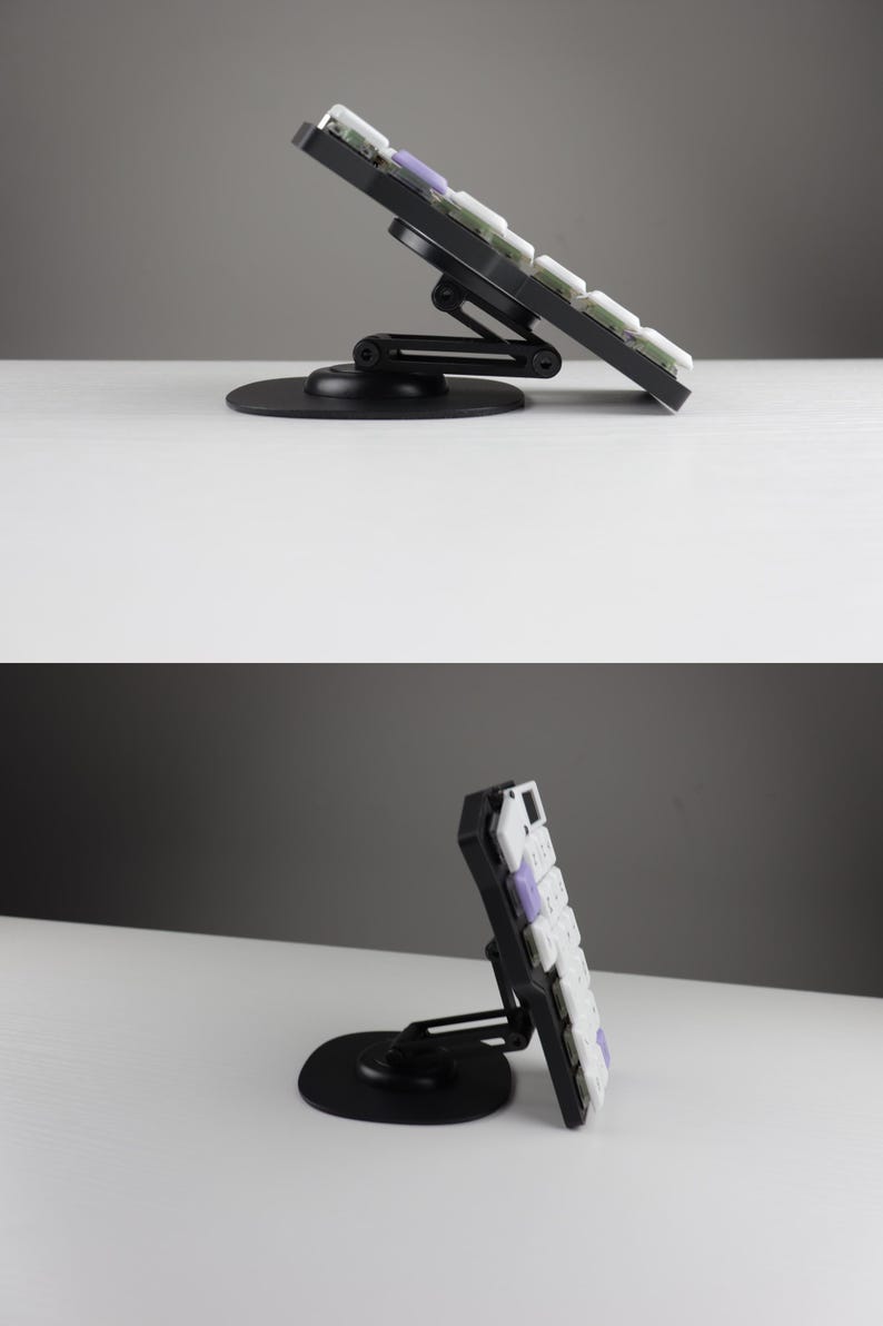 May include: A black mechanical keyboard with white and purple keycaps is mounted on an adjustable black stand. The stand has a circular base and a hinged arm, allowing for tilt adjustment. The keyboard is angled upwards.