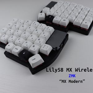 Puede incluir: Un teclado mecánico ergonómico dividido con teclas blancas, base negra y un módulo de panel táctil gris. El texto Lily58 MX Wireless, ZMK y MX Modern está impreso en la esquina. Las teclas presentan letras y símbolos negros sobre fondo blanco.