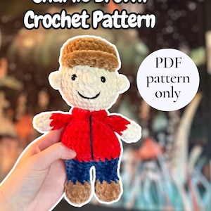 May include: A handmade crochet doll of Charlie Brown, featuring a white face, brown hair and hat, a red jacket, blue pants, and brown shoes. The image includes the text "Charlie Brown Crochet Pattern" and "PDF pattern only".
