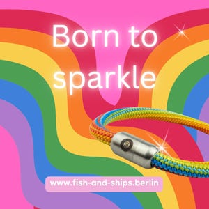 Op de afbeelding: Een regenboogkleurige touwarmband met een cilindervormige zilverkleurige magnetische metalen sluiting met een klein logo. De tekst Born to sparkle staat boven de armband en www.fish-and-ships.berlin staat onderaan.