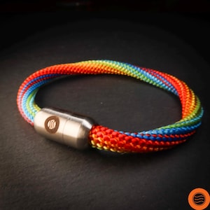 Pode incluir: Uma pulseira de corda arco-íris com fecho magnético prateado. A pulseira é feita de fios coloridos e bem tecidos em um espectro de cores. O fecho apresenta um design circular. Circunferência de aproximadamente 18 cm.